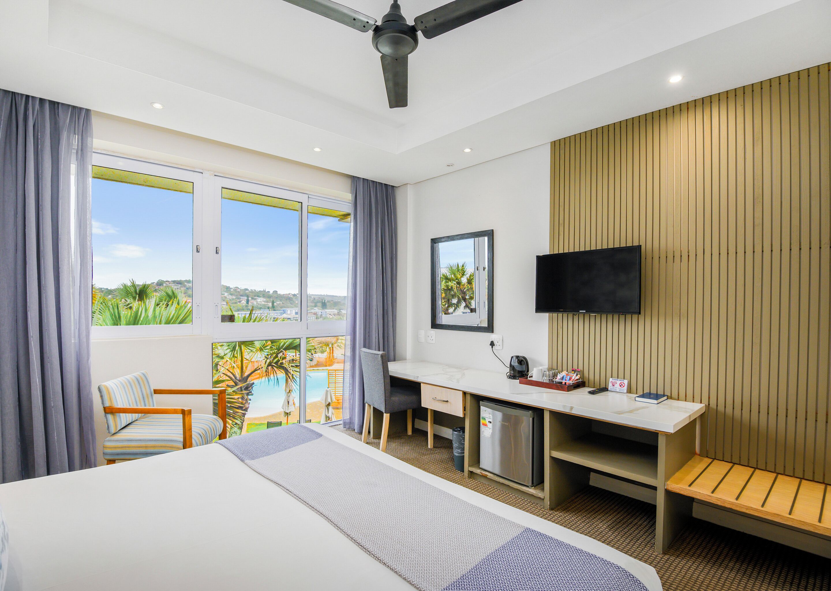 Habitación de hotel con cama, escritorio, silla, televisor y vistas al exterior.