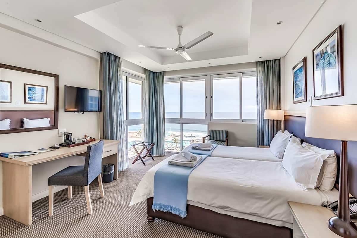 Habitación de hotel con cama, escritorio, silla, televisor y ventanas grandes con vistas.