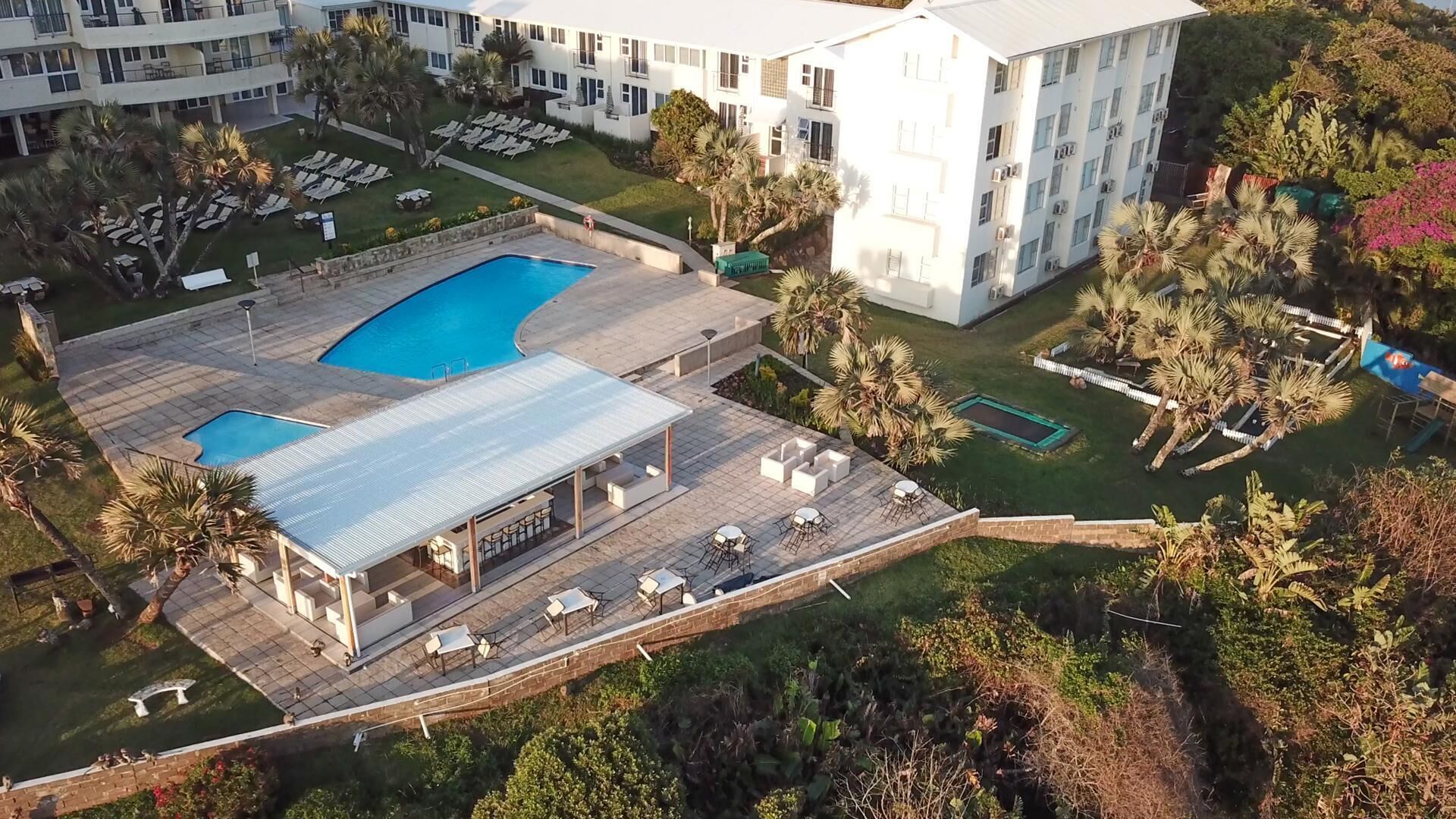 Eine Luftaufnahme eines Resorts mit einem großen Pool, Sitzgelegenheiten im Freien und üppiger Bepflanzung.