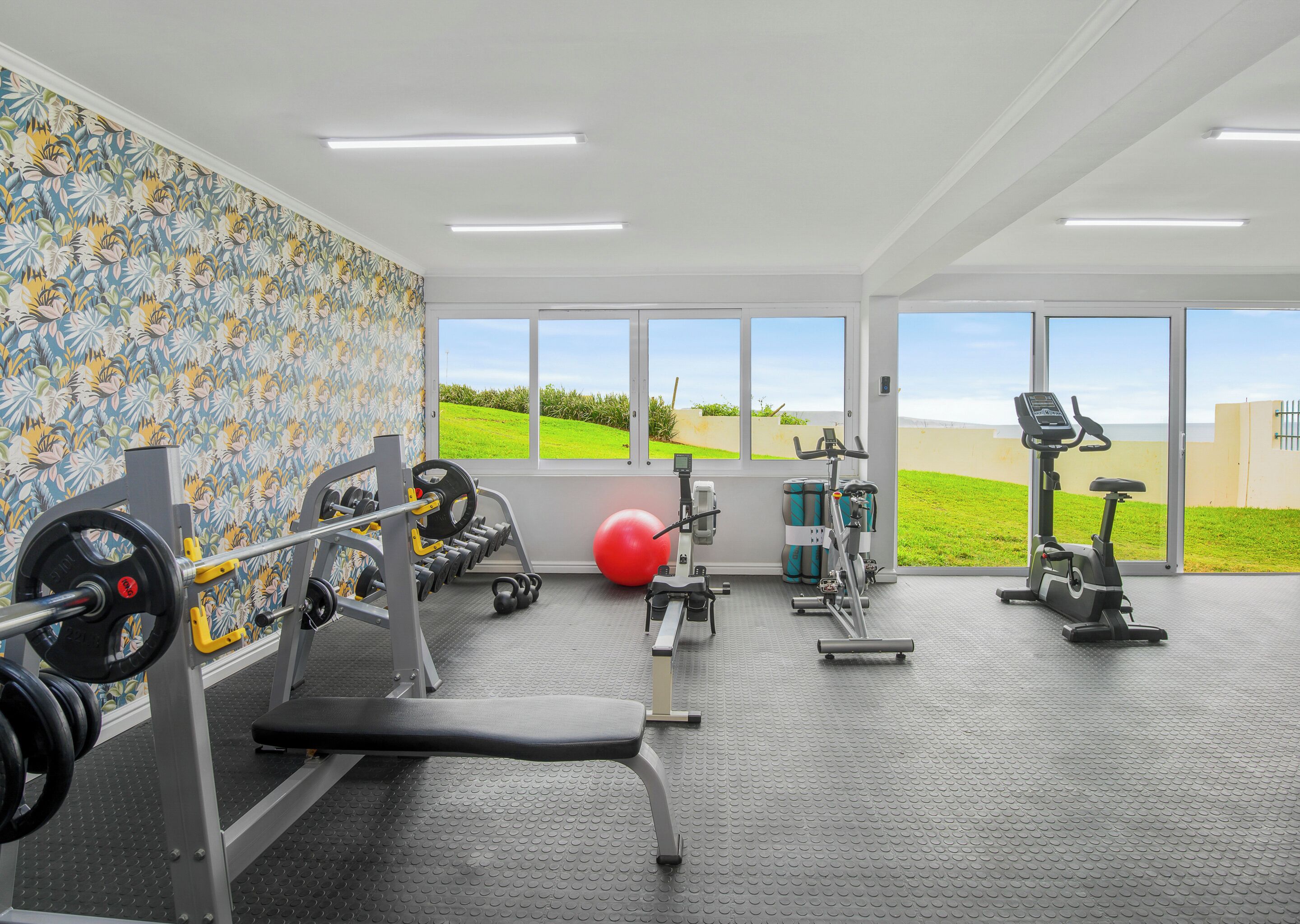 A gym with various exercise equipment, large windows, and a view of a green field.