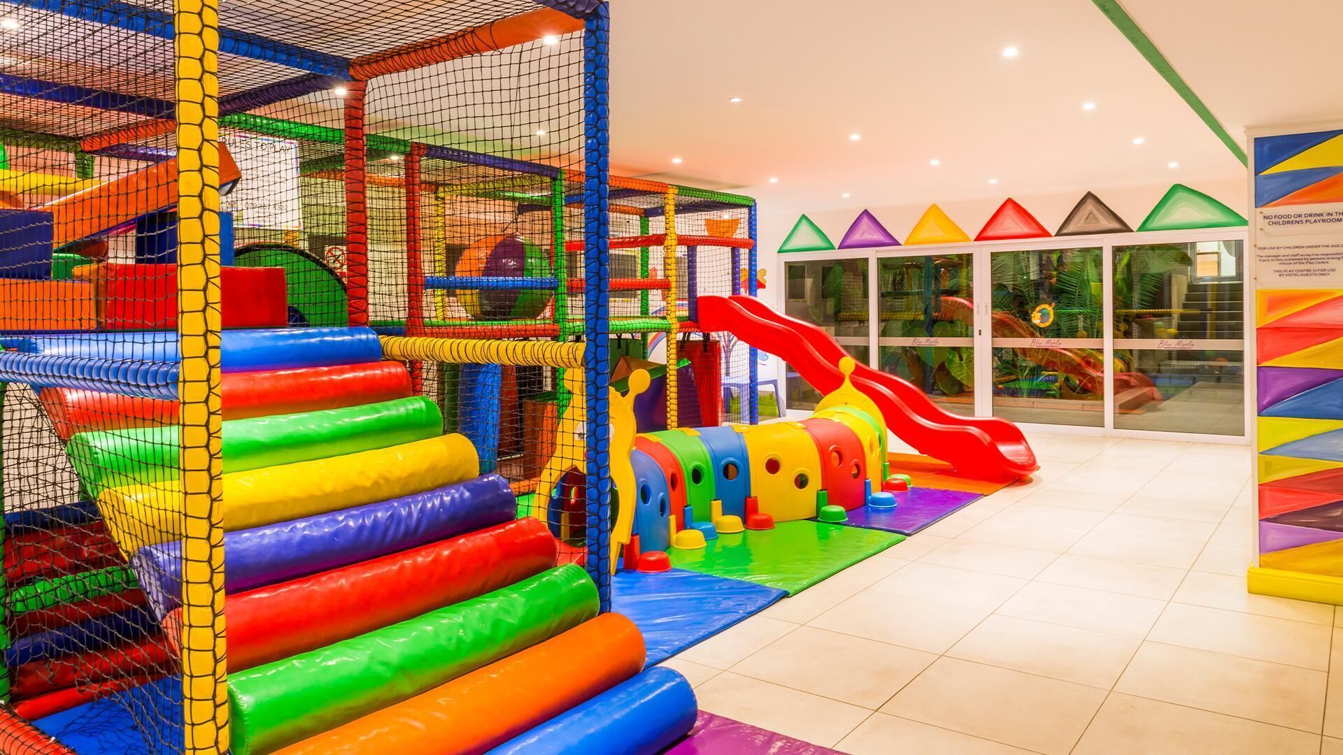 An indoor play area with a netted climbing structure, a slide, and colorful play equipment.