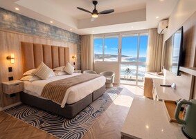 Quarto de hotel moderno com uma cama grande, uma escrivaninha, uma cadeira e vista para o oceano.