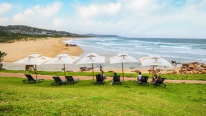 A beachside view with multiple white umbrellas labeled "DREAM Hotels & Resorts" and black lounge chairs arranged in rows. - Blue Marlin All-Inclusive Seascape by Dream Resorts (Scottburgh)