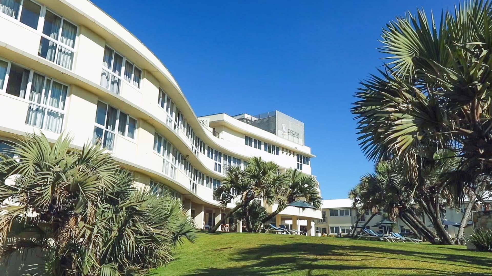 A modern hotel with a curved facade, palm trees, and a clear blue sky.