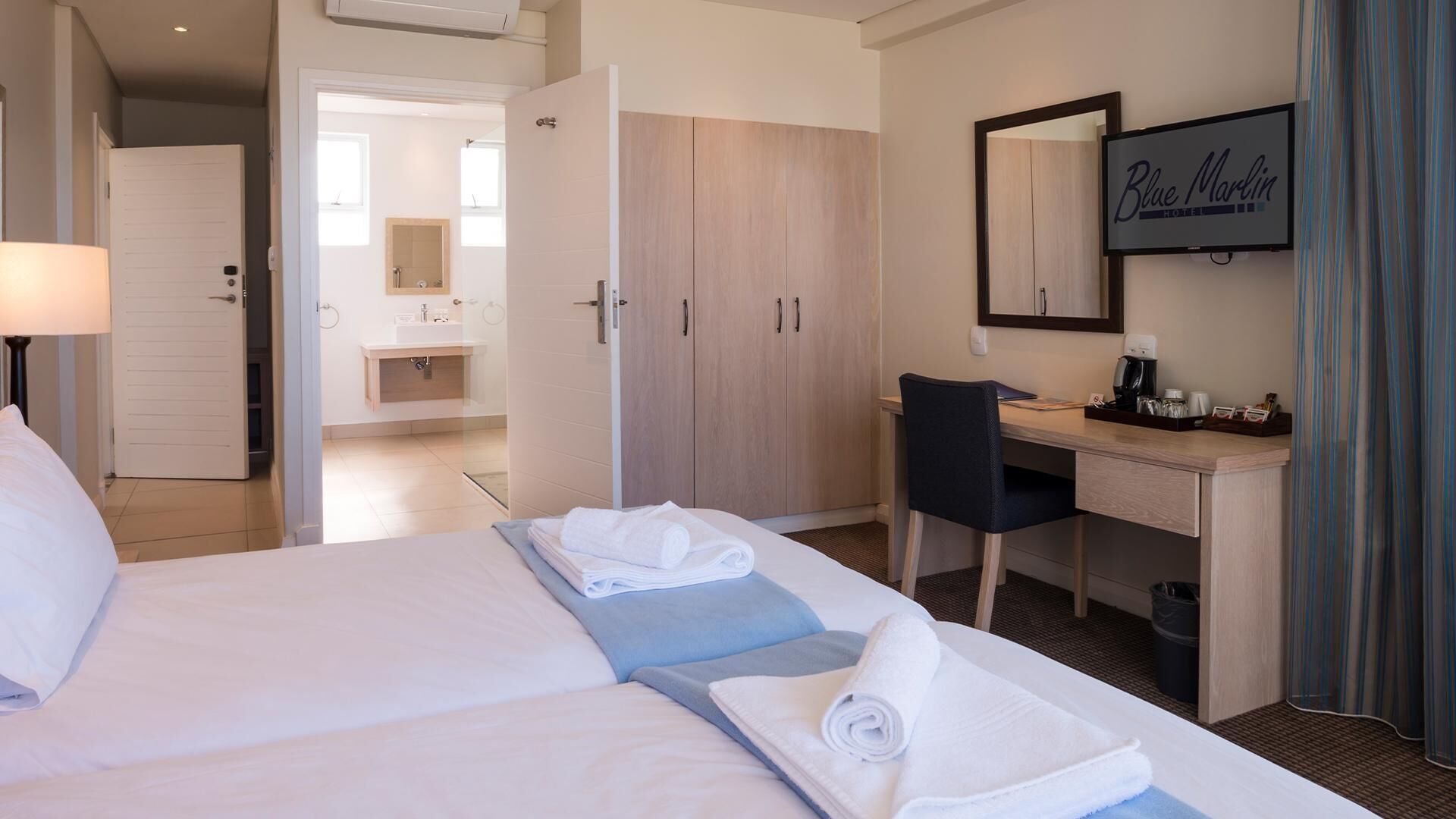 A hotel room with a bed, a desk, a chair, a bathroom with a mirror, and a television on the wall.