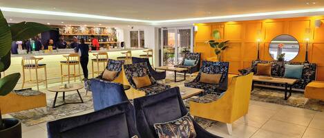 A hotel lobby with a bar area, seating with floral upholstery, and a large mirror on the wall.