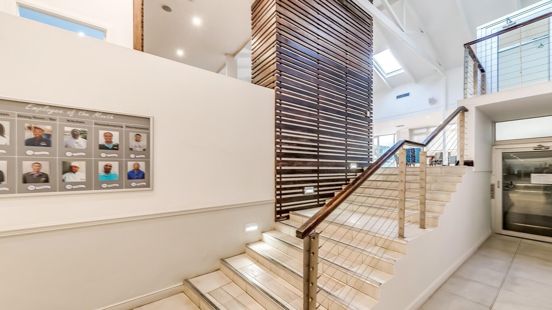 A modern hotel interior with a staircase, a framed photo display, and a kitchen area.