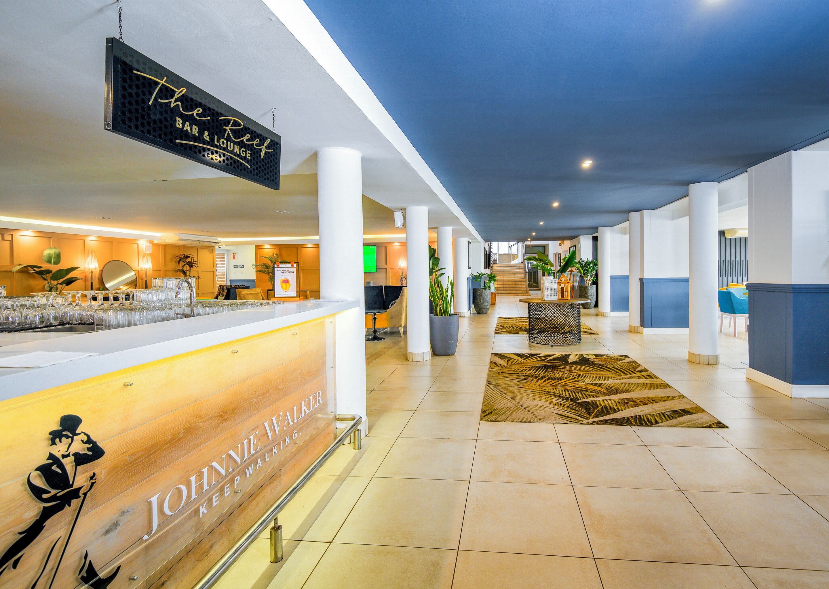 A hotel lobby with a reception desk, a bar/lounge area, and a staircase leading to upper floors.