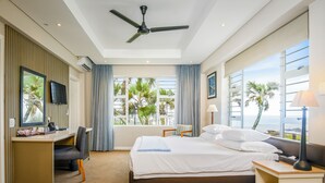 A hotel room with a bed, desk, chair, and a view of palm trees and the ocean. - Blue Marlin All-Inclusive Seascape by Dream Resorts (Scottburgh)