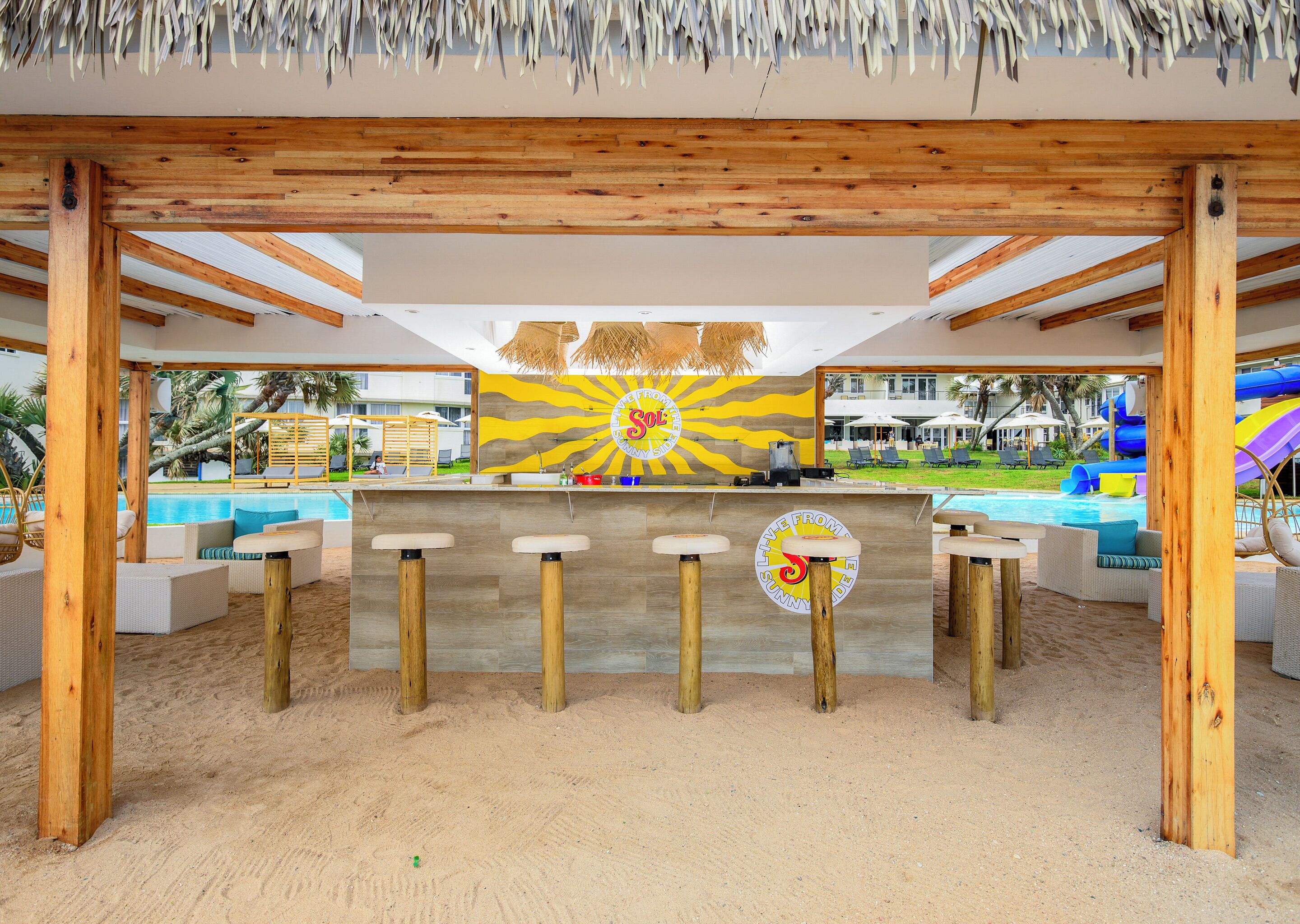 A beachside bar area with wooden pillars, a pool, and a colorful mural.
