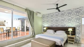A hotel room with a bed, a ceiling fan, a nightstand, a lamp, a window with curtains, and a view of the outdoor area.