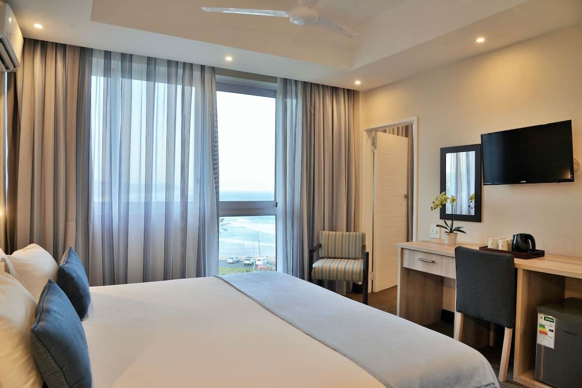 Habitación de hotel con una cama grande, un escritorio con silla, televisión y vista al océano.