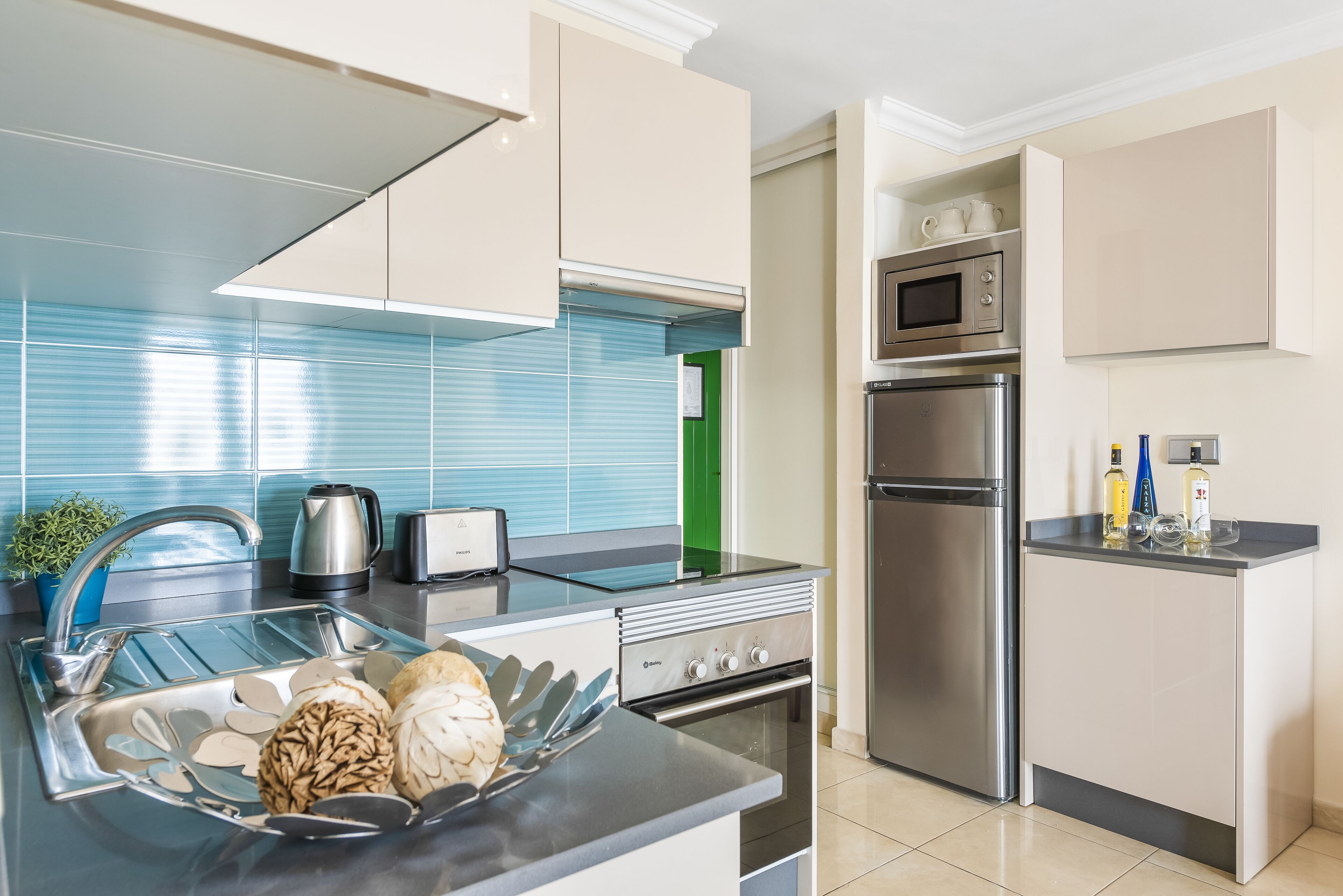 A modern kitchen with stainless steel appliances, a glass-top island, and a green accent wall.