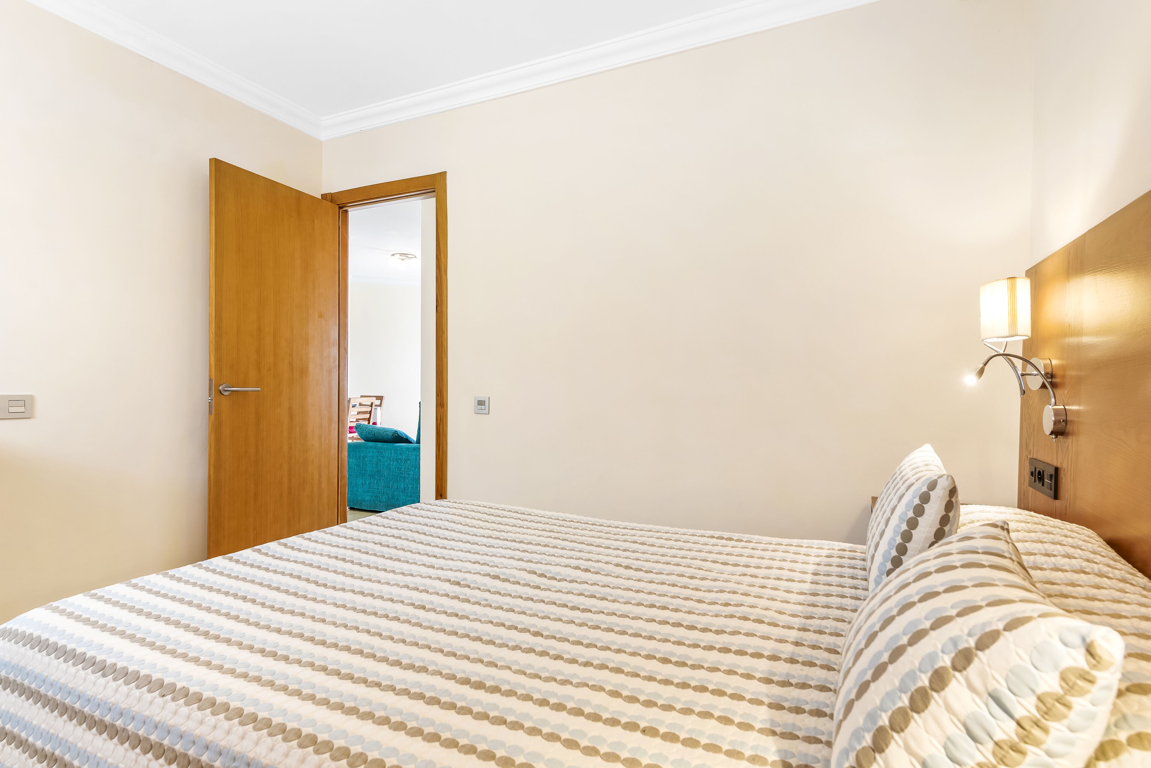 A bedroom with a bed, a wooden door, and a wall-mounted light fixture.