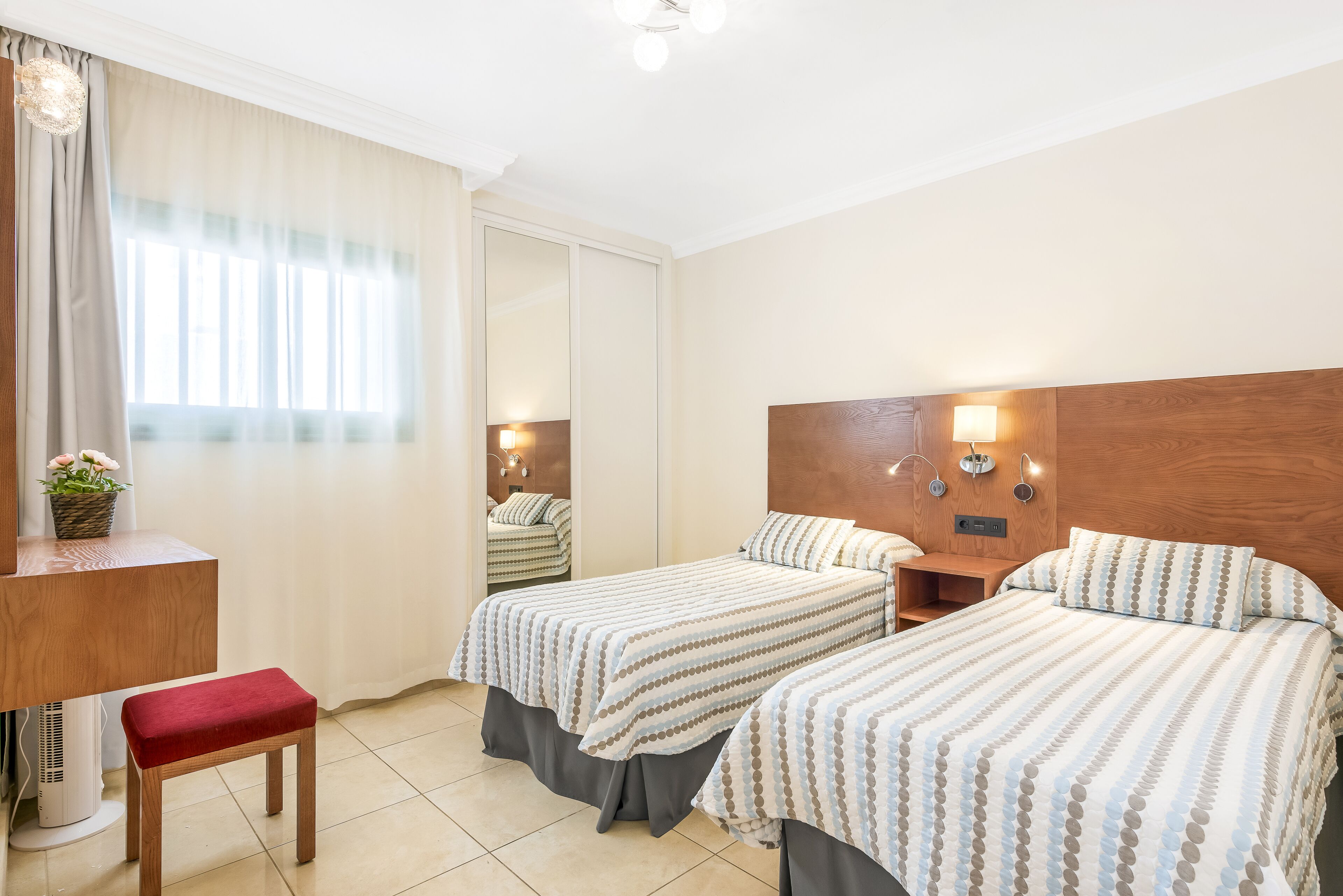 A hotel room with two beds, a desk, a chair, and a mirror.