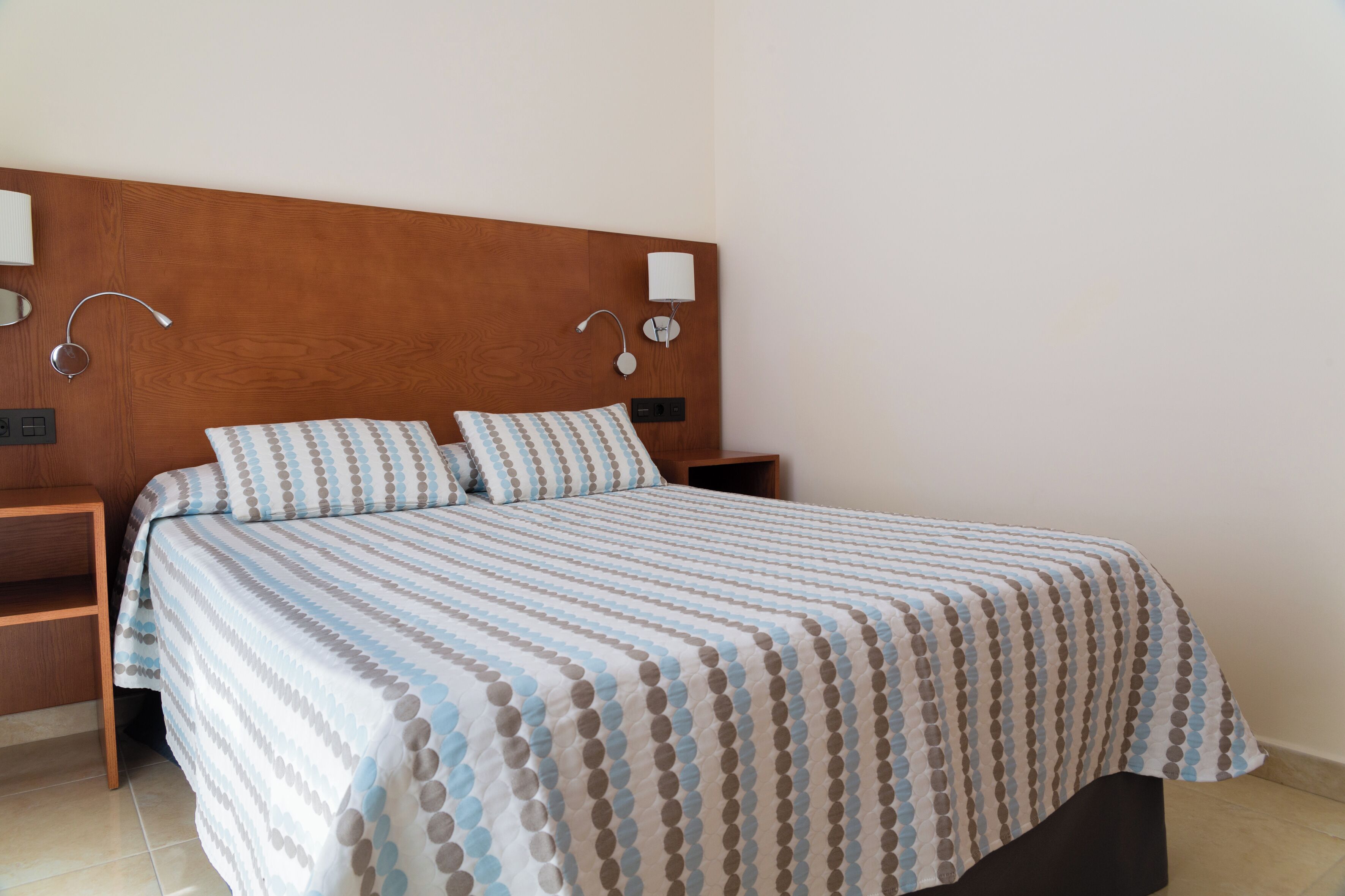 A neatly made bed with a striped bedspread, two bedside tables with lamps, and a wooden headboard.