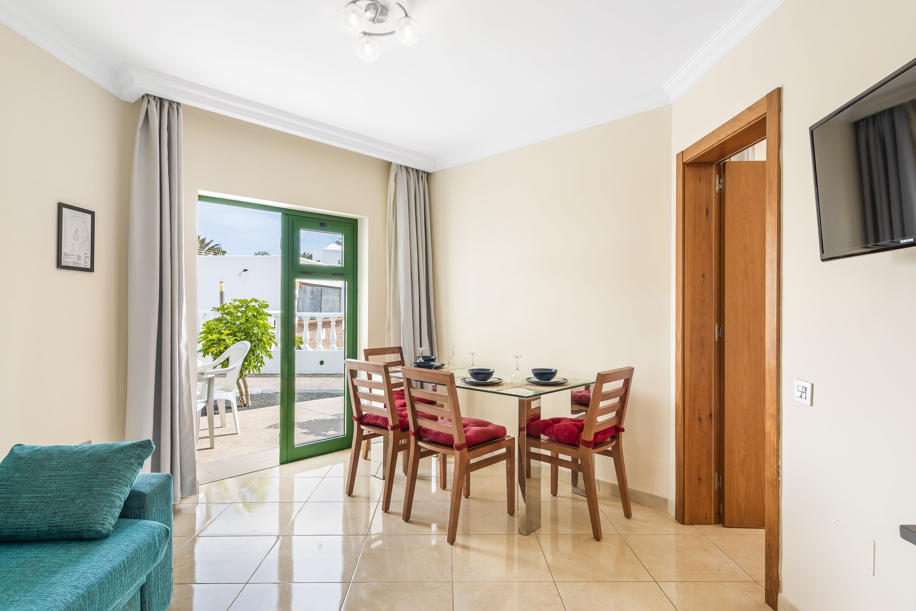 A dining area with a glass table, wooden chairs, and a view through a glass door to an outdoor patio.