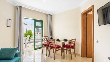 A dining area with a glass table, wooden chairs, and a view through a glass door to an outdoor patio.