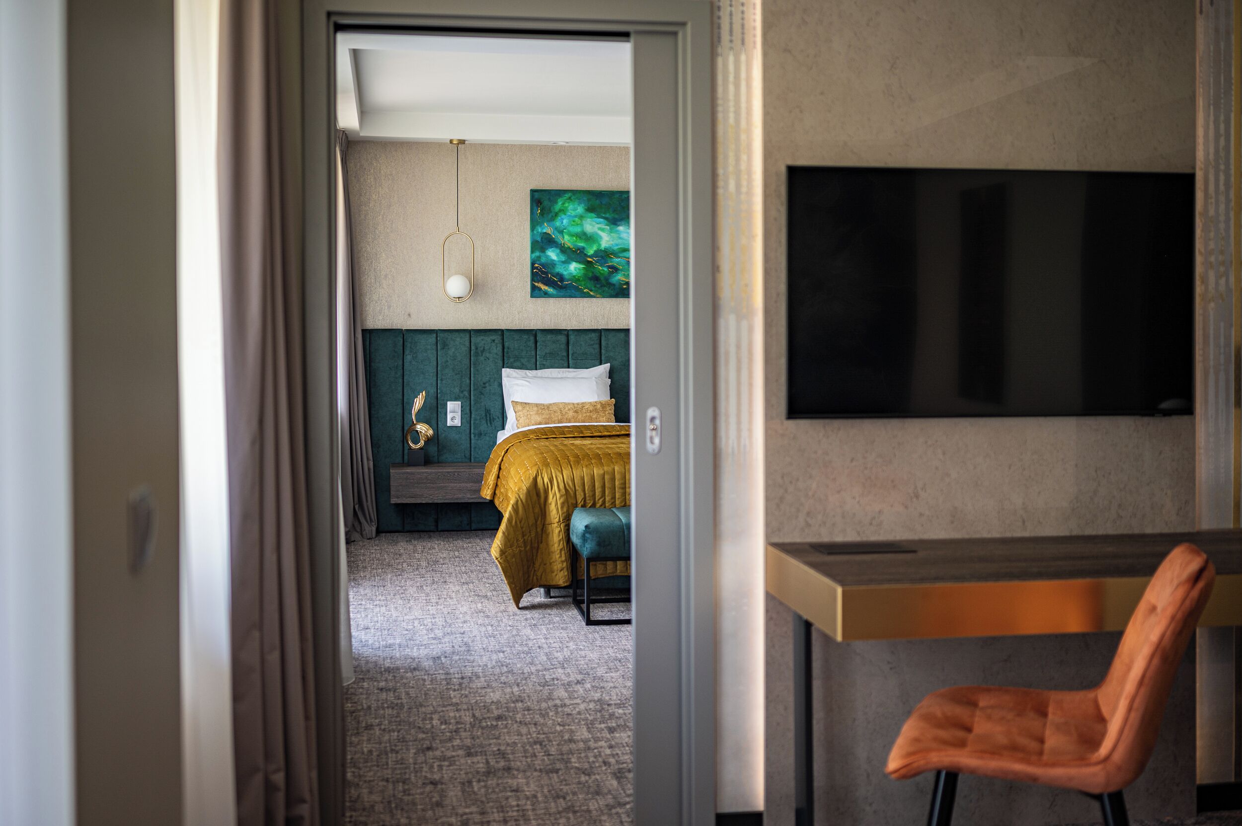 A hotel room with a bed, a desk, a chair, a television, and a painting on the wall.
