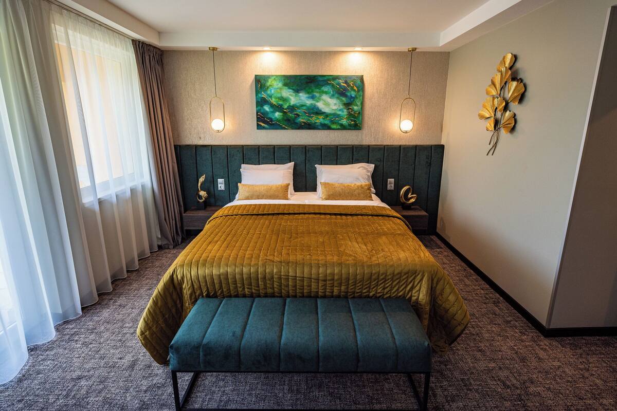A hotel room with a bed, a bench, a painting, and a wall decoration.