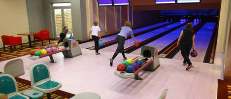 A bowling alley with lanes, bowling balls, and a few people playing.