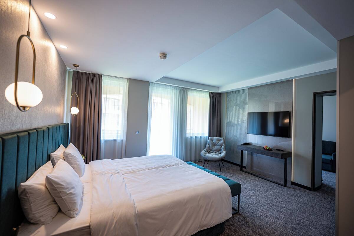 A modern hotel room with a large bed, a desk, a chair, and a TV.