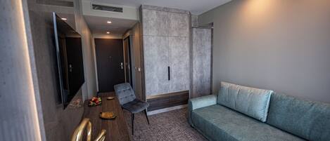 A modern hotel room with a grey sofa, a wooden side table, a flat-screen TV, and a wall-mounted cabinet.