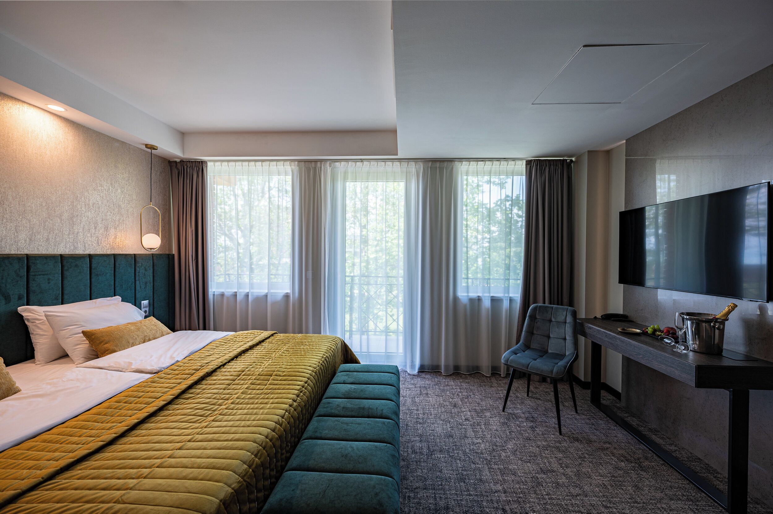 A hotel room with a bed, a desk, a chair, a TV, and a window with curtains.