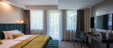 A hotel room with a bed, a desk, a chair, a TV, and a window with curtains.