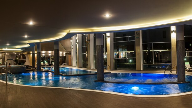 An indoor swimming pool with multiple lanes, surrounded by lounge chairs and a modern architectural design. - Hotel Azúr Prémium (Siófok)