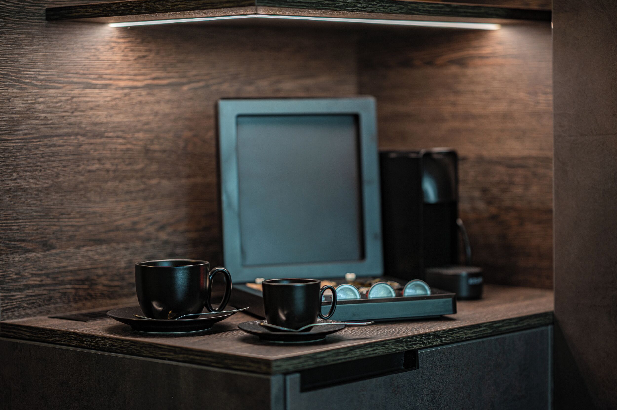 A wooden counter with two black cups and a tray of coffee pods.