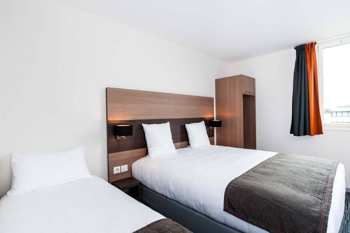 Una habitació d'hotel amb dos llits, un panell de fusta al capçal, làmpades laterals i una finestra amb cortines.