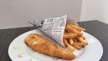 A plate with a fish and chips meal, including a newspaper and fries.