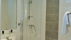 Ein modernes Badezimmer mit einer gläsernen Duschkabine, einem weißen Waschbecken und einem großen Spiegel.