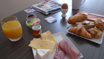 Een ontbijttafel met sinaasappelsap, kaas, ham, croissants en een krant.