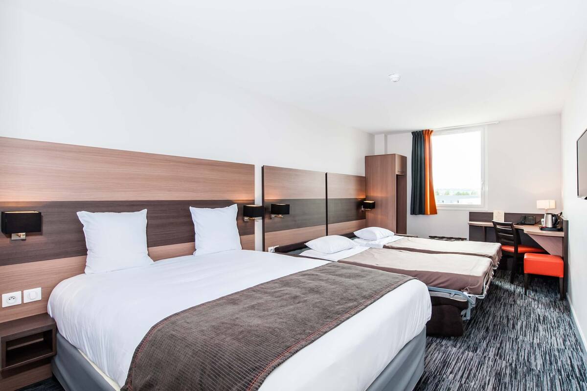 Una habitació d'hotel amb dos llits, una taula de treball, una cadira i una finestra amb cortines.
