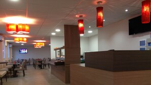 Ein Restaurant mit Holztischen und -stühlen, einer Theke und roten Hängelampen.
