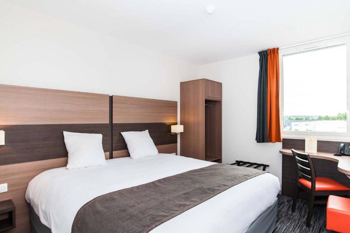 Una habitació d'hotel amb un llit, un escriptori i una cadira. Hi ha una finestra amb cortines.