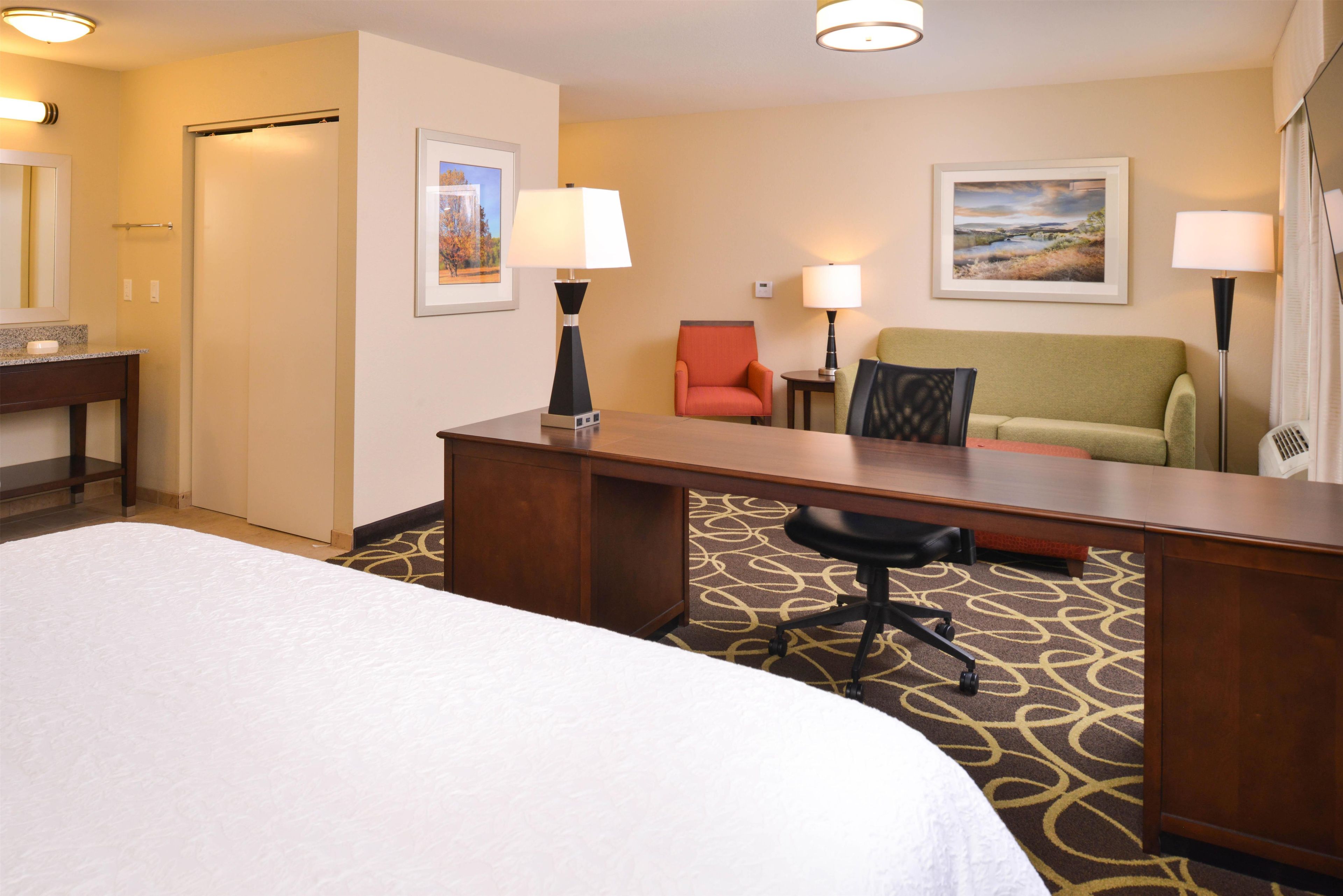 A hotel room with a bed, desk, two chairs, a sofa, and two lamps.
