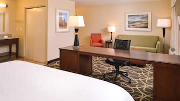 A hotel room with a bed, desk, two chairs, a sofa, and two lamps.