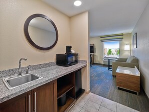 A hotel room with a granite countertop, a sink, a microwave, a coffee maker, a mirror, a small seating area with a chair and a table, and a window with a view. - Hampton Inn Omaha Midtown-Aksarben Area (Omaha)