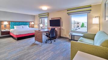 A hotel room with a bed, desk, chair, TV, and windows.
