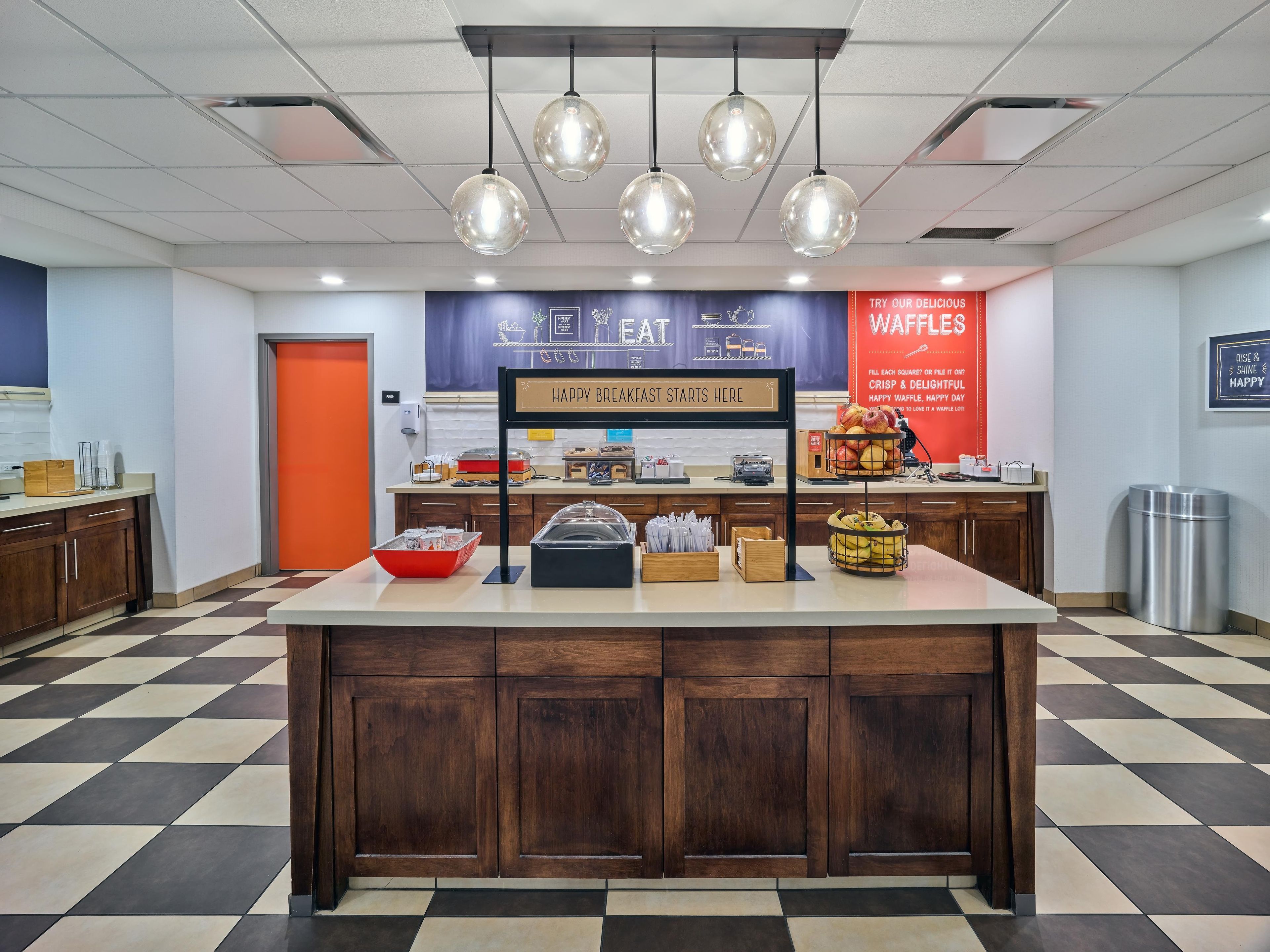 A breakfast area with a counter, food display, and a waffle sign.