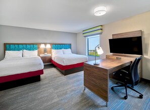 A hotel room with two beds, a desk with a TV, a chair, a window with a view, and a nightstand with a lamp. - Hampton Inn Omaha Midtown-Aksarben Area (Omaha)