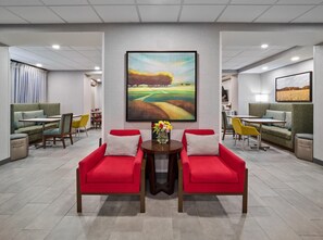 A modern lobby with two red armchairs, a table with flowers, and a large landscape painting on the wall. - Hampton Inn Omaha Midtown-Aksarben Area (Omaha)