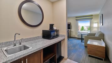 A hotel room with a kitchenette, a sink, a microwave, and a seating area with a view.
