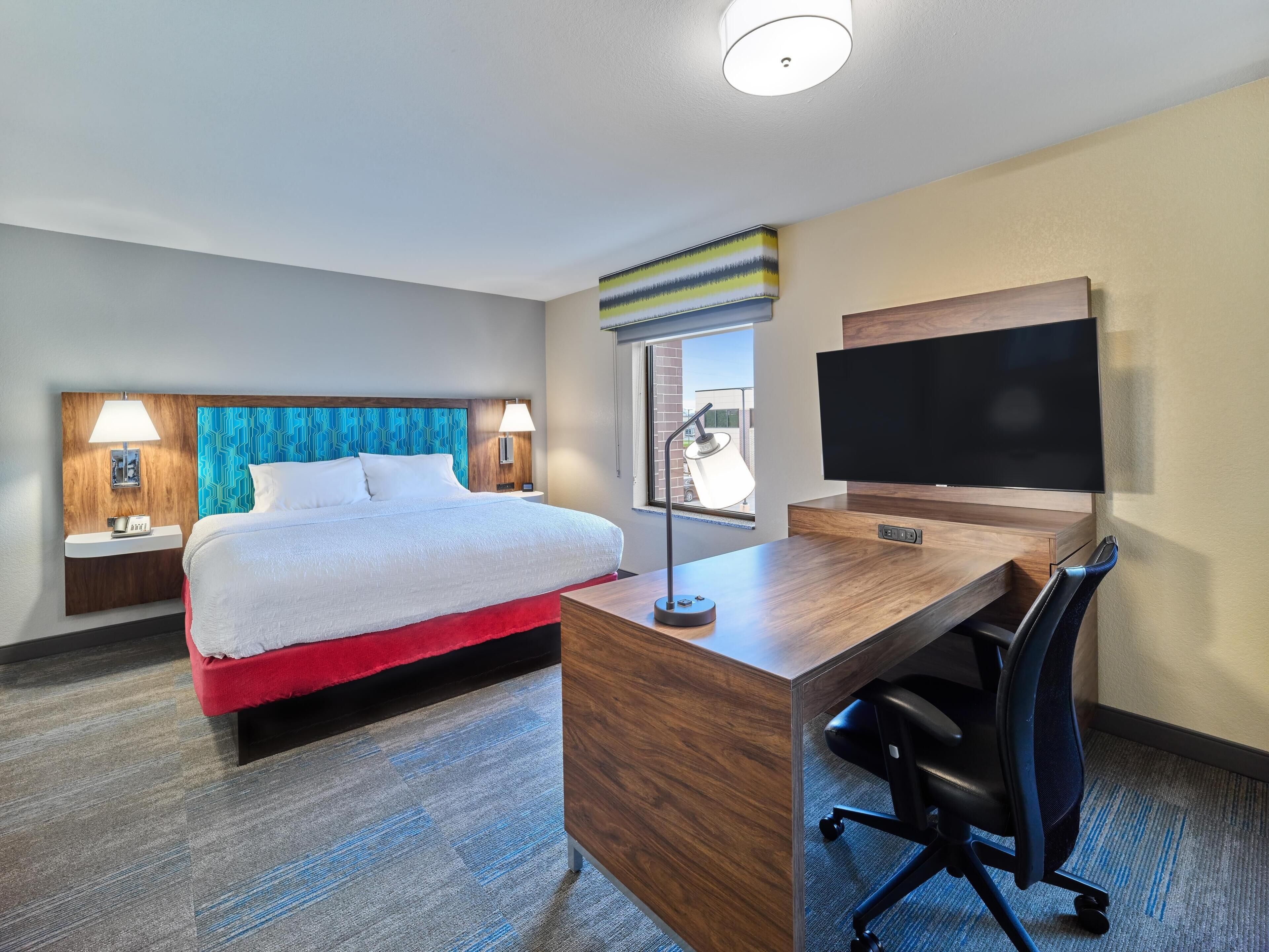 A hotel room with a bed, desk, chair, TV, and a window with a view.