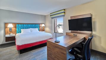 A hotel room with a bed, desk, chair, TV, and a window with a view.