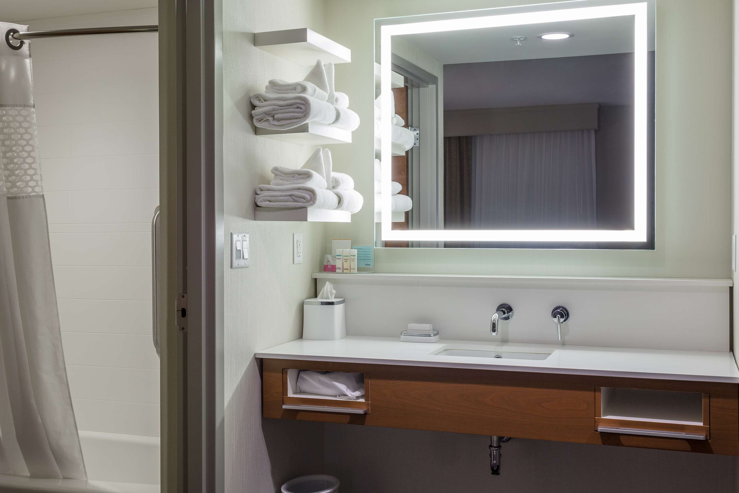 Un baño moderno con tocador, espejo con iluminación integrada y toallas dobladas ordenadamente en un estante.