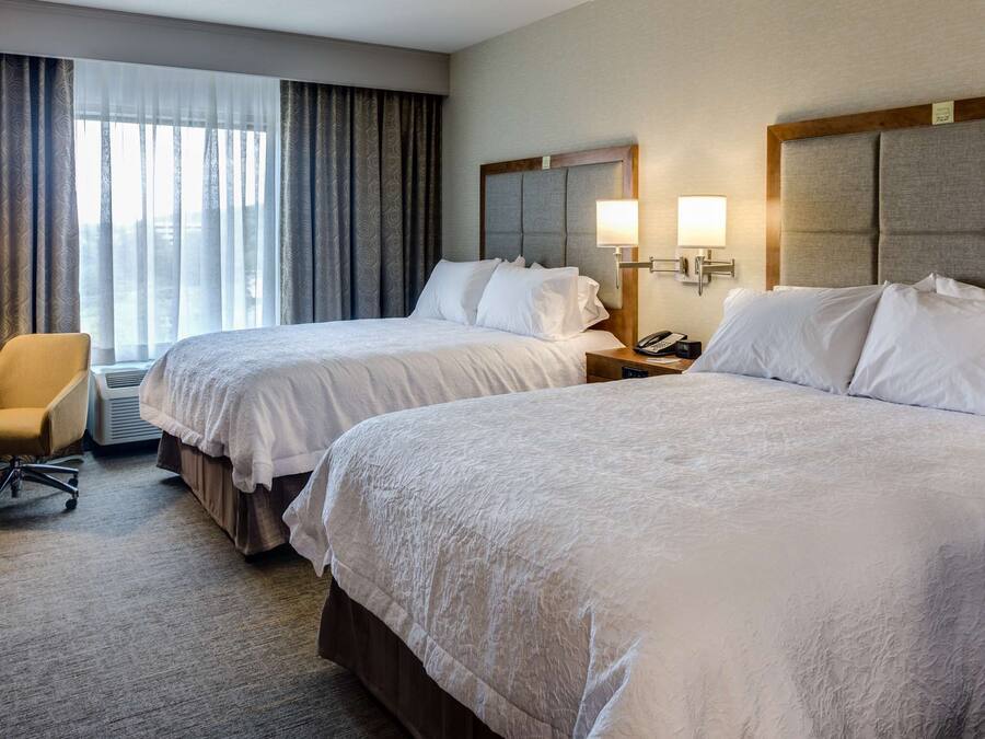 A hotel room with two beds, a desk, a chair, and a TV.